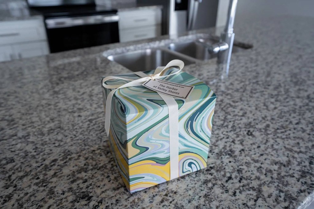 A gift box with a white ribbon is on a granite countertop.