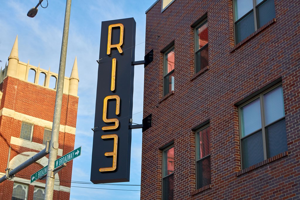 A sign for RISE is hanging next to a street sign.
