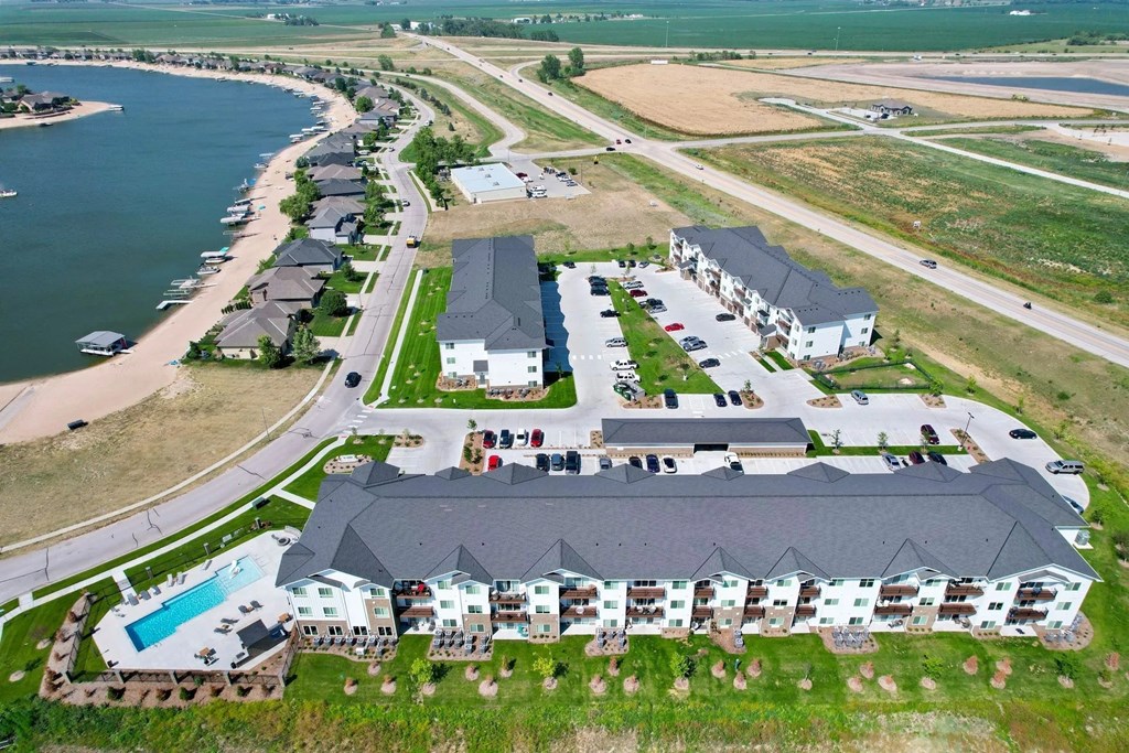 A large building with a pool is surrounded by a grassy area and a road.