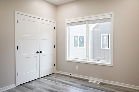 A room with a white door and a window with white blinds.