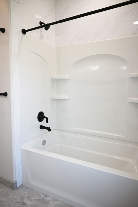 A white bathroom with a tub and shelves.