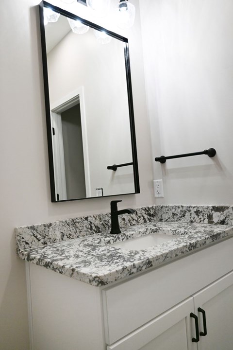 A bathroom with a marble countertop and a mirror above it.