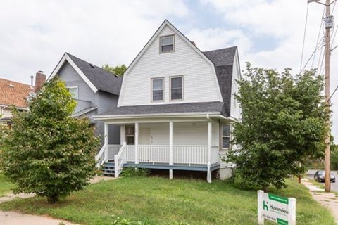 A two-story house with a porch and a sign in front.