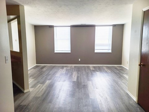 A room with wooden flooring and two windows with blinds.