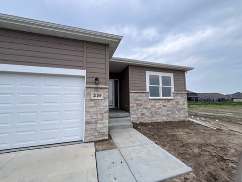 A house with a brown siding and a white garage door is numbered 21209.