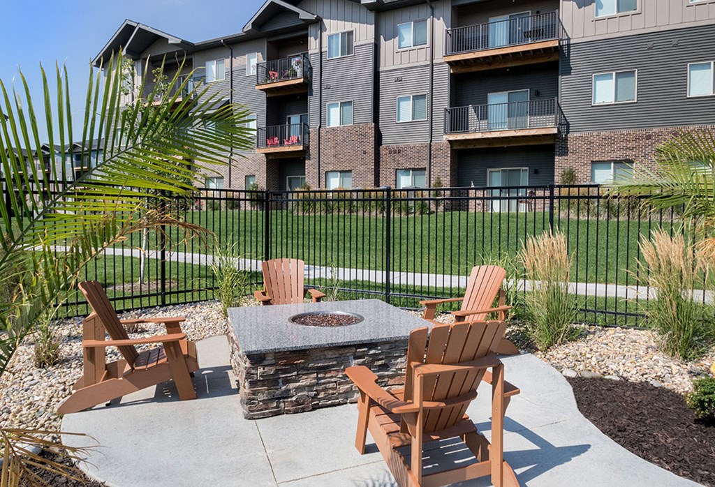A patio with chairs and a fire pit in front of a brick building.