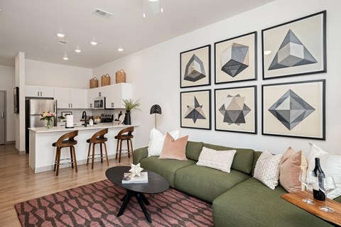 A living room with a green couch and a coffee table in front of a wall with framed geometric art.