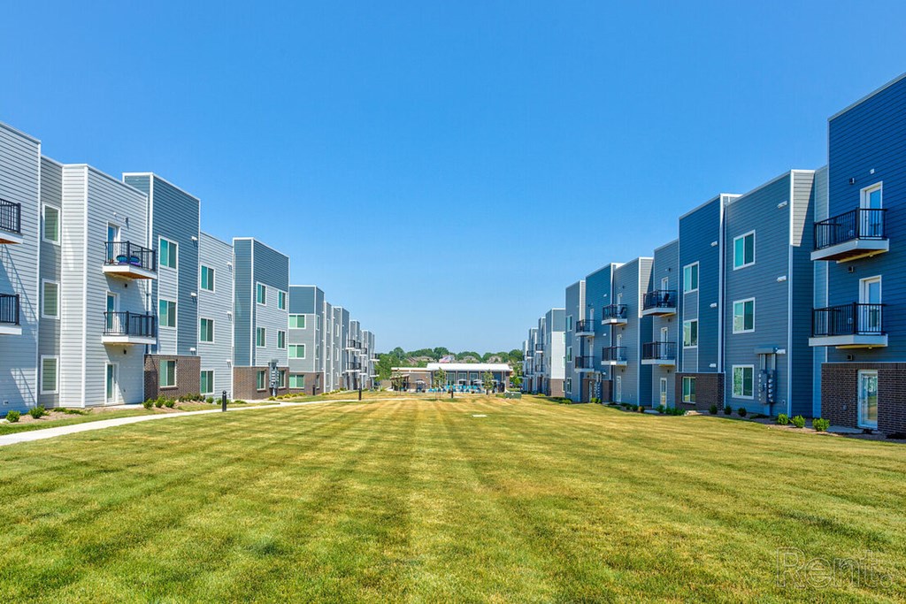 A row of modern apartment buildings with a grassy lawn in the foreground at Lofts at Fox Ridge, Raymore, MO, 64083