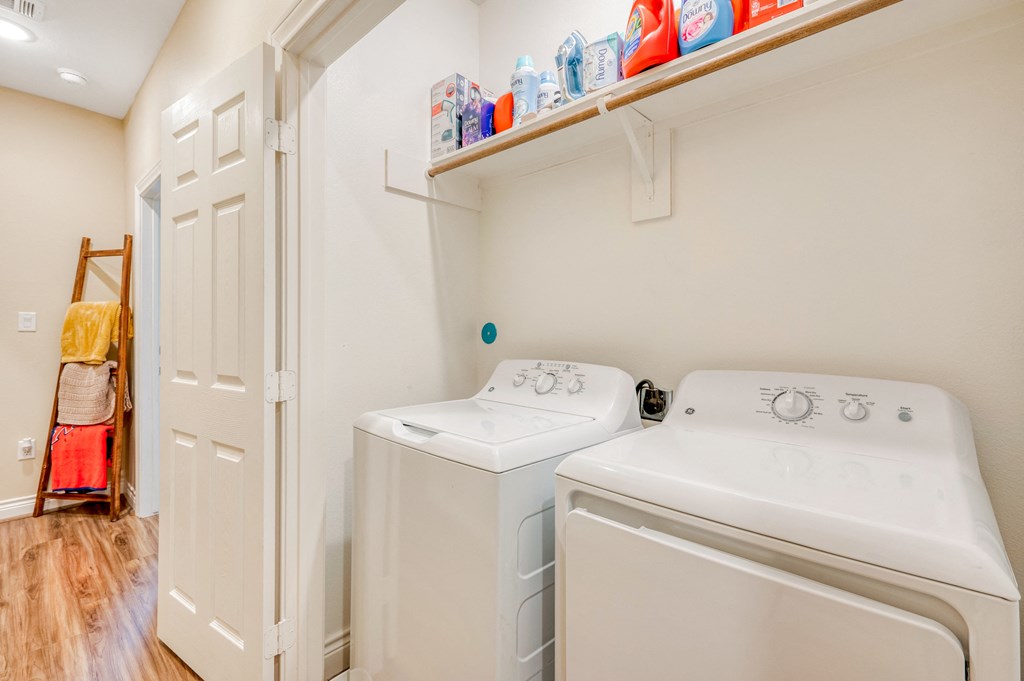 a washer and dryer in a white laundry room with a shelf above it