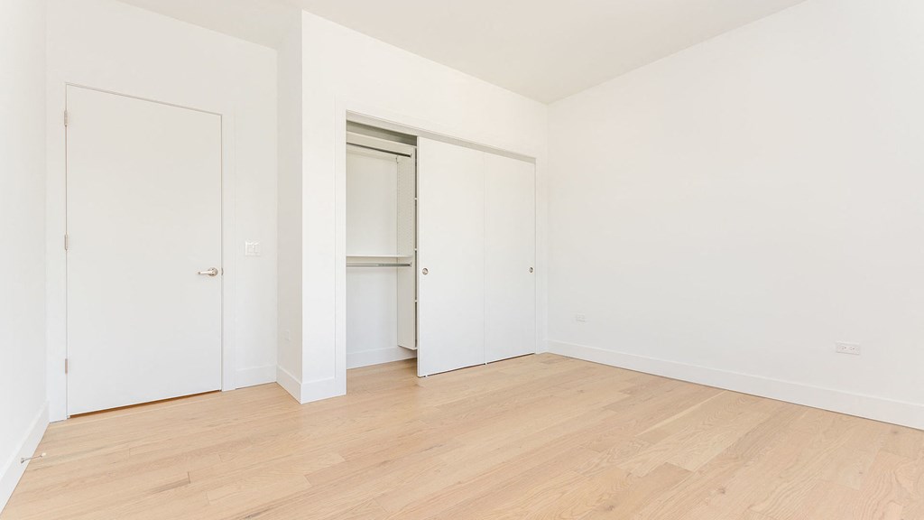 a bedroom with white walls and wood floors and a closet