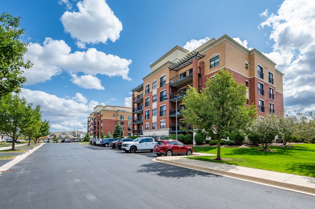 A red car is parked on the side of a street in front of a large apartment building.