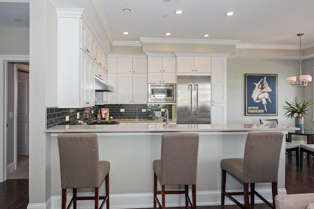 a kitchen with white cabinets and a bar with chairs