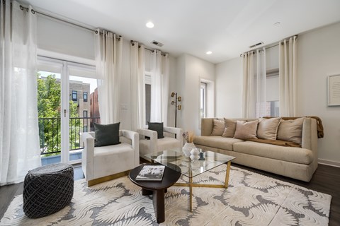A living room with a white sofa, a black ottoman, and a glass coffee table.