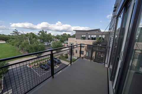 A balcony with a black railing and a parking lot in the background.