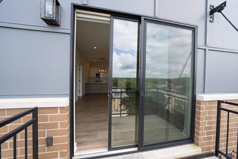 A glass door with a black frame is open, revealing a room with a wooden floor and a white wall.