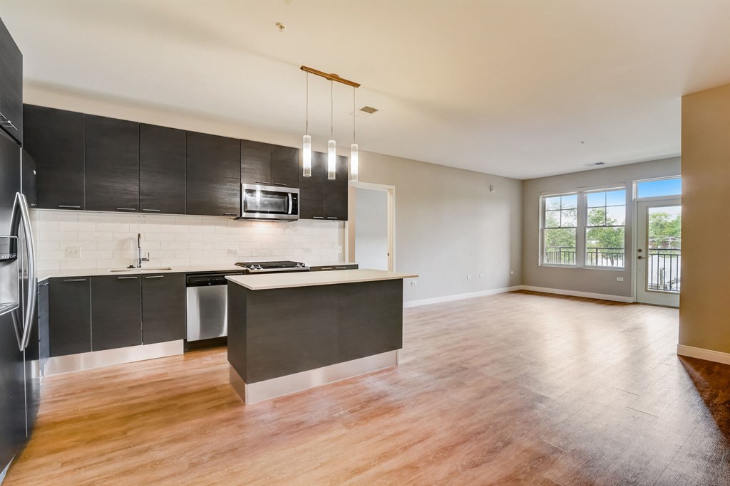 an empty kitchen and living room with wood floors and black cabinets at Clarendon Hills 229, Clarendon, IL