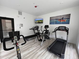 a gym with various exercise equipment on the floor and a tv on the wall