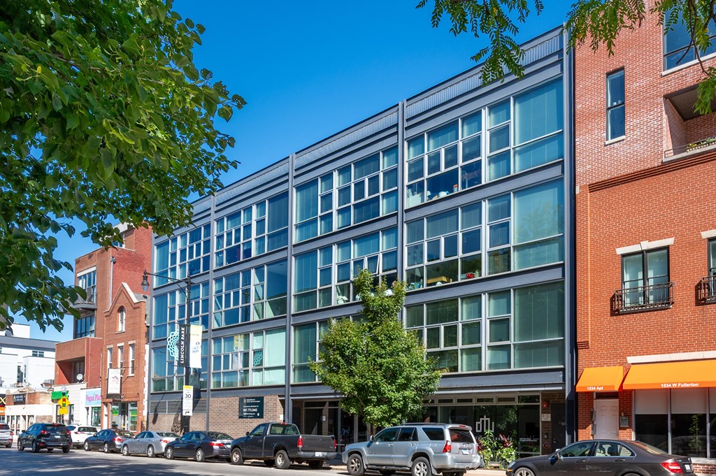 A modern glass building is situated on a street corner with cars parked in front.