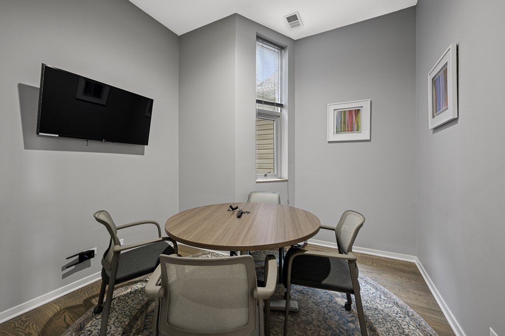 A conference room with a table, chairs, and a television mounted on the wall.