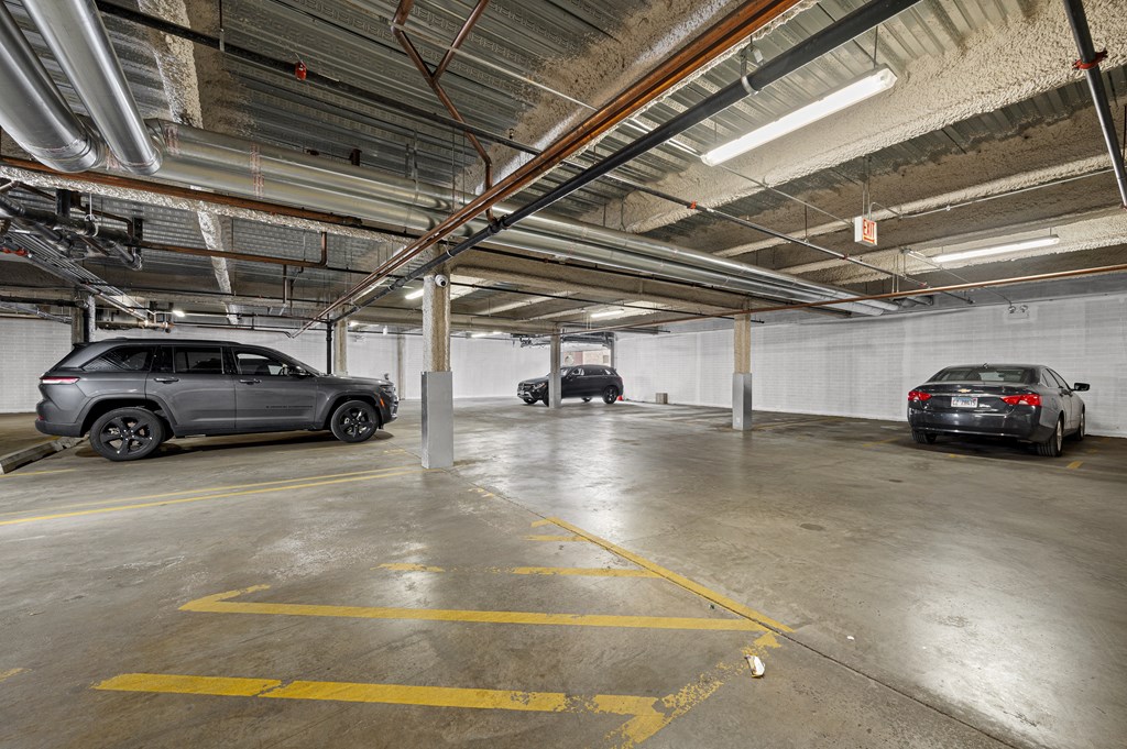 A parking garage with a grey car in the foreground and a black car in the background.