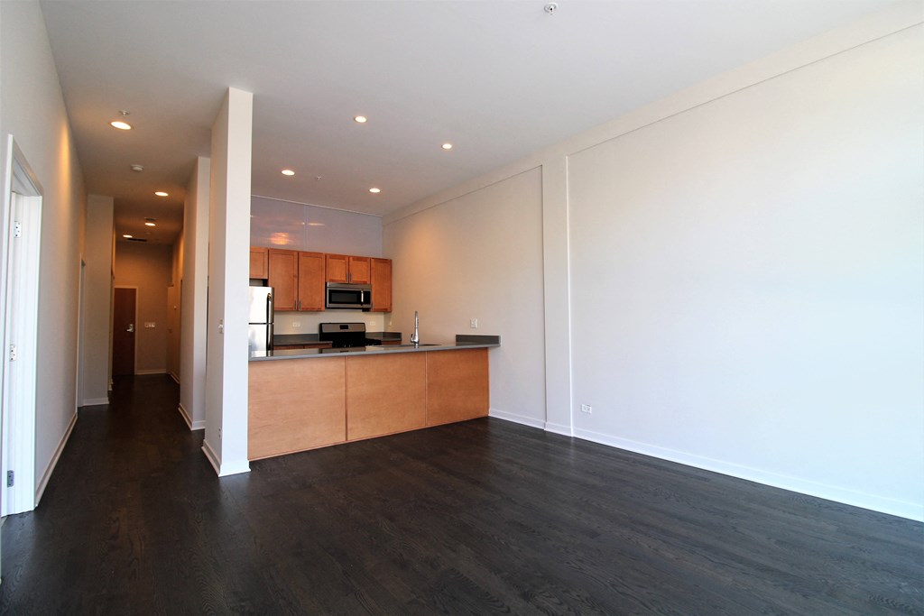 an empty living room and kitchen with wood floors and white walls