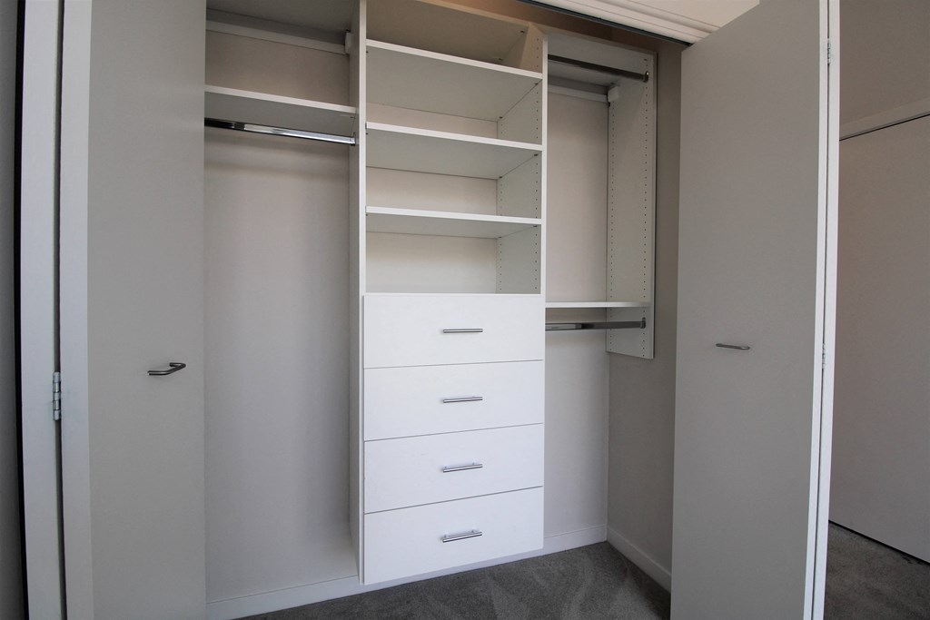 a walk in closet with white cabinets and drawers