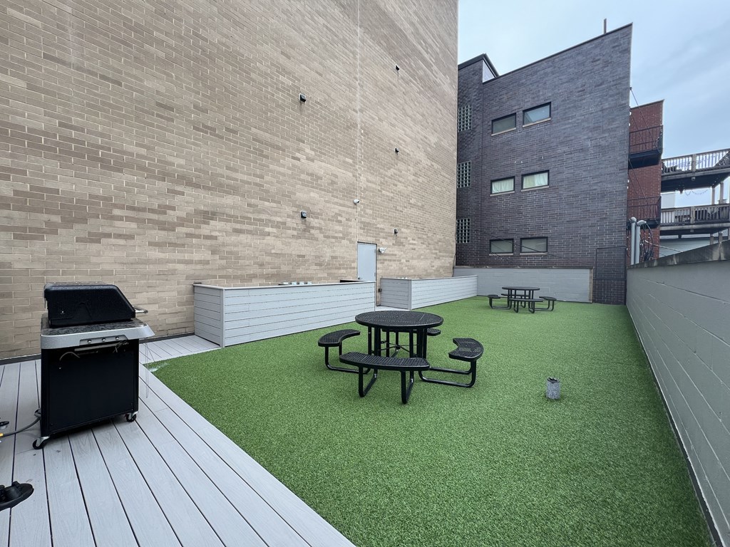 a roof deck with a grill and a table and chairs on a green turf