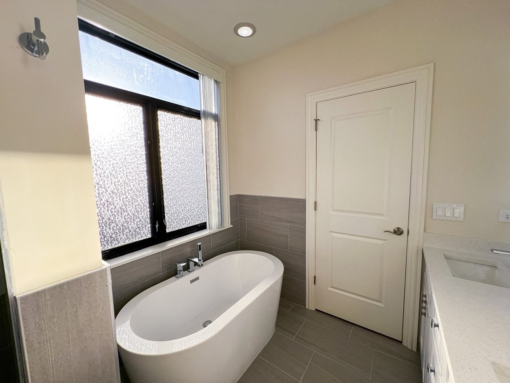 A white bathroom with a tub, sink, and window.