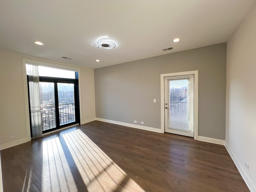 A spacious room with wooden flooring and a large window with a view of a cityscape.