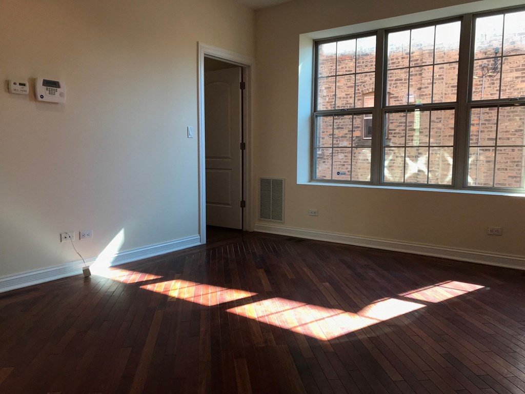 an empty living room with wood floors and a large window at Tripp 4321, Chicago