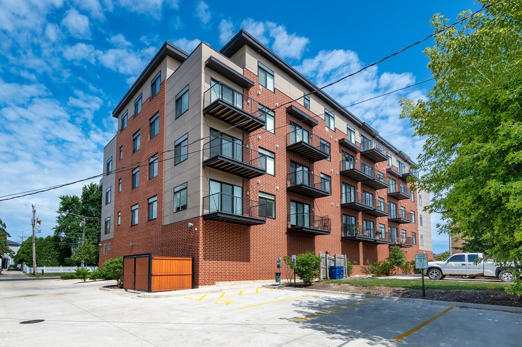 A large red brick apartment building with a parking lot in front.