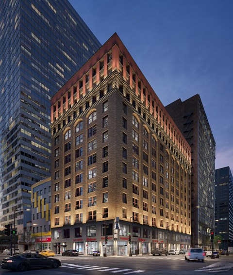 A large, multi-story building with a red brick facade is situated between two modern glass buildings.