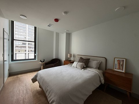 A bedroom with a large bed and a window overlooking a city.