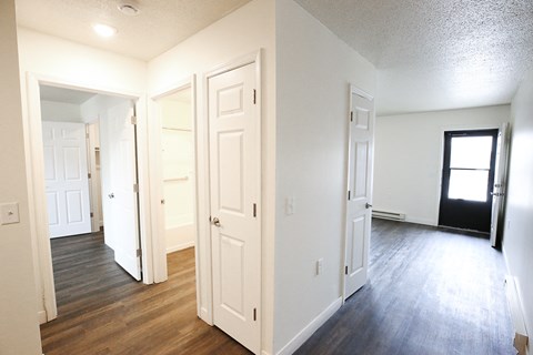 A room with white walls and wooden floors with a door open to another room.