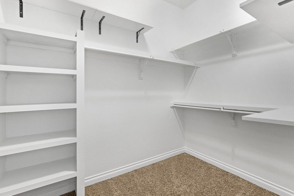 a walk in closet with white shelving and empty shelves