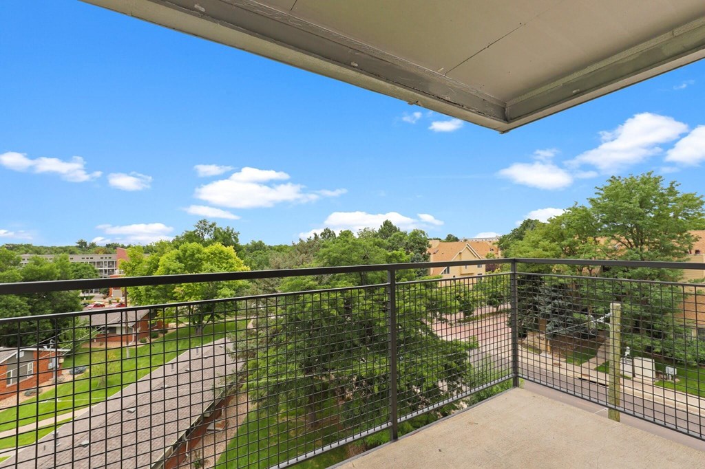 A balcony with a black railing overlooks a green lawn and a brick building  at 4805 E Kentucky in Denver, CO