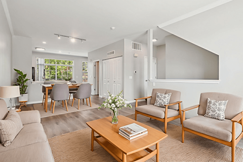 A living room with a grey couch, a wooden coffee table, and a dining table with chairs.