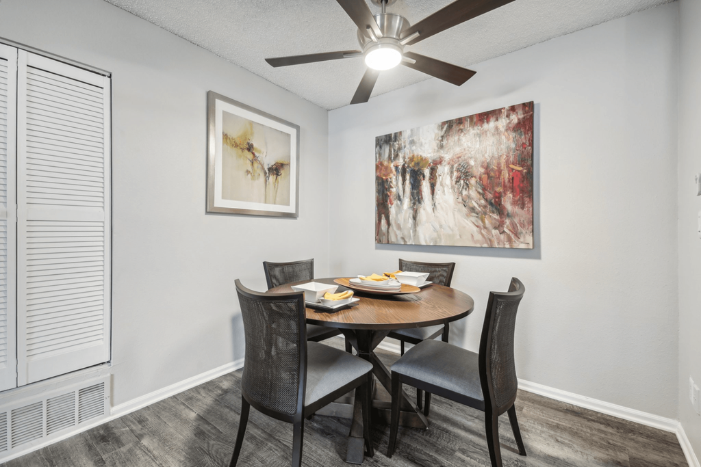 A dining room with a table set for two and a ceiling fan.