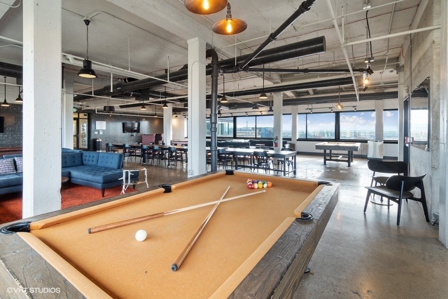 A pool table is in the middle of a room with a couch and chairs at Archer Tower in Denver, CO