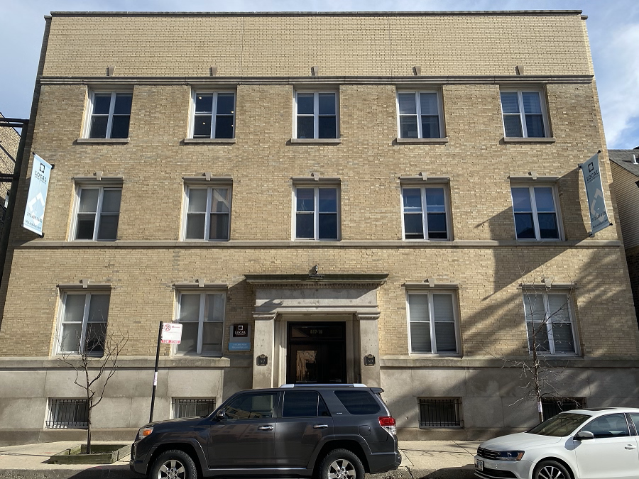 A grey SUV is parked in front of a tan building.