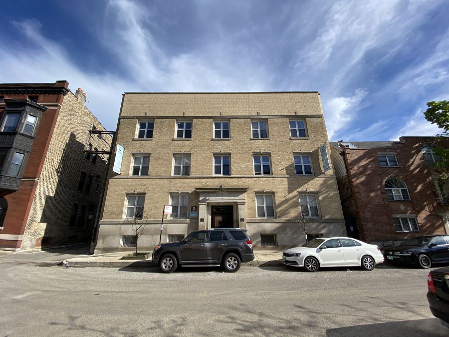A grey car is parked in front of a tan building.