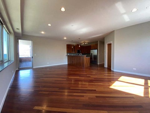 A spacious room with wooden flooring and a kitchen area in the background.