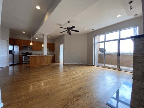 an empty living room with a kitchen and a ceiling fan