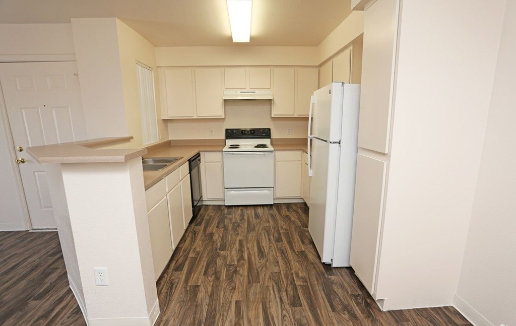 Open kitchen with wood-like flooring and white appliances at Canon de Arrowhead in Albuquerque, New Mexico