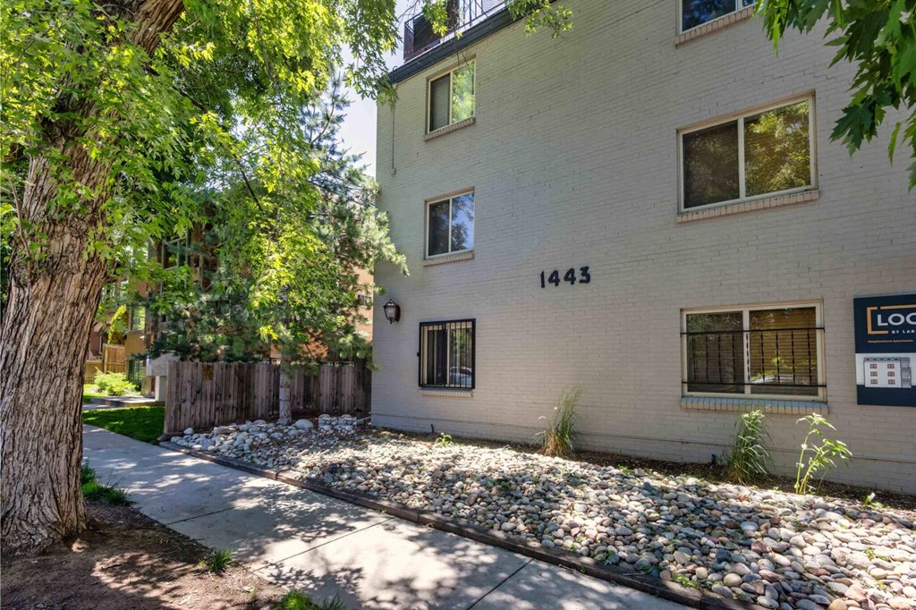 the side of a white house with trees and a sidewalk