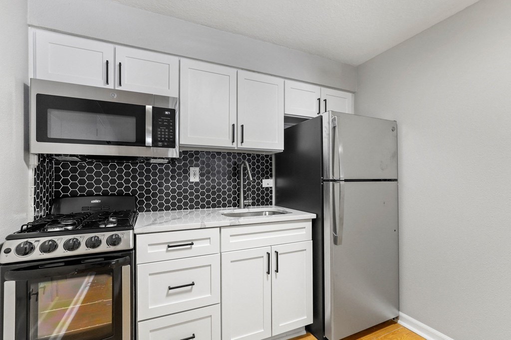 A kitchen with a black refrigerator, white cabinets, and a black and white tiled backsplash at 1355 Pearl in Denver, CO