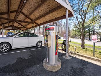 Covered car care station with a free-standing vacuum and parking spaces, located under a wooden canopy in a tree-lined lot.