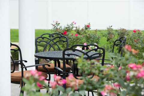 A table and chairs are set in a garden with flowers.