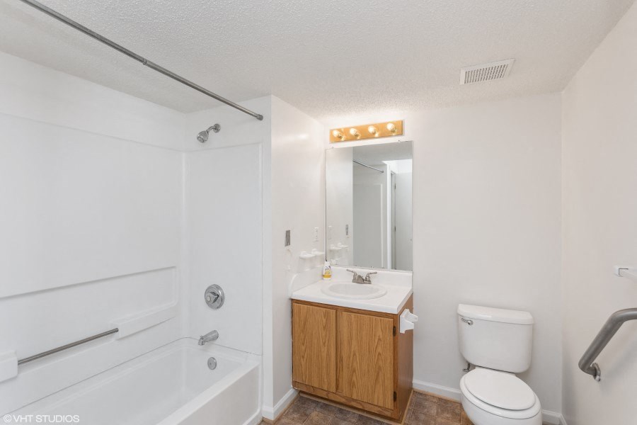 A white bathroom with a wooden cabinet under a mirror.