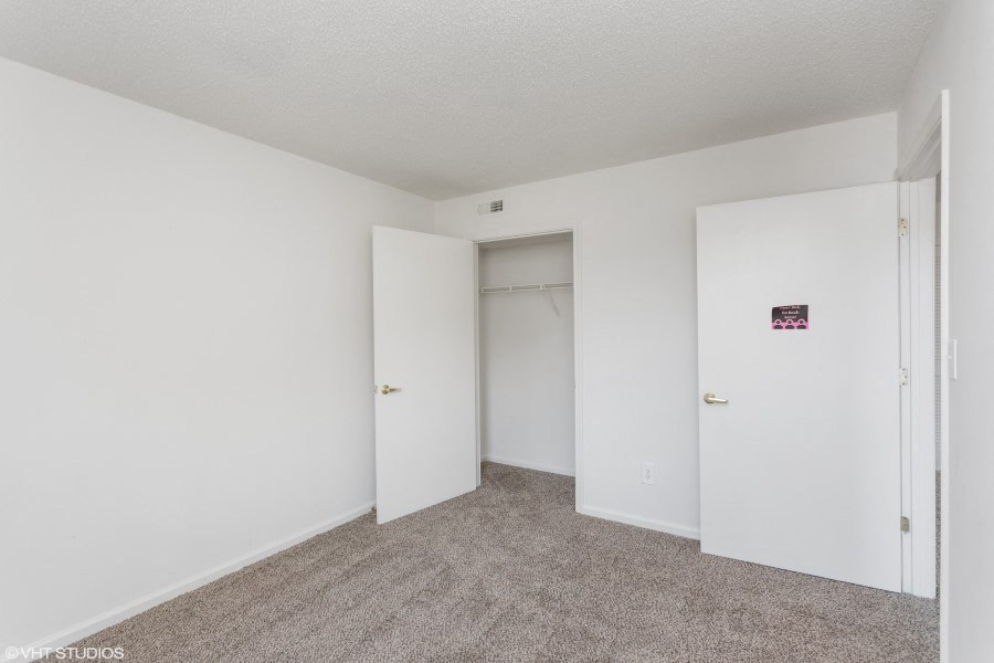 A room with white walls and carpeted floor with two doors.